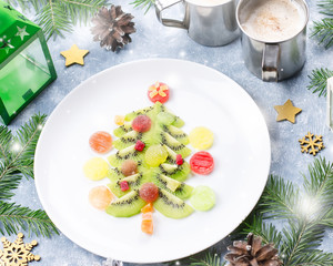 Christmas tree made of kiwi and fruit jelly on a plate with fir branches and decorations. Top view, copy space