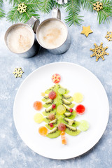 Christmas tree made of kiwi and fruit jelly on a plate with fir branches and decorations. Top view, copy space