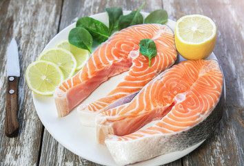 Two pieces of fresh salmon steak on a white plate with spinach and lemon, on  a gray wooden background. Omega 3 vitamin, healthy lifestyle. Natural vegetarian food. Top view.