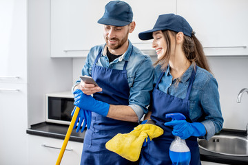 Man and woman as a professional cleaners in uniform standing together with phone during the break...