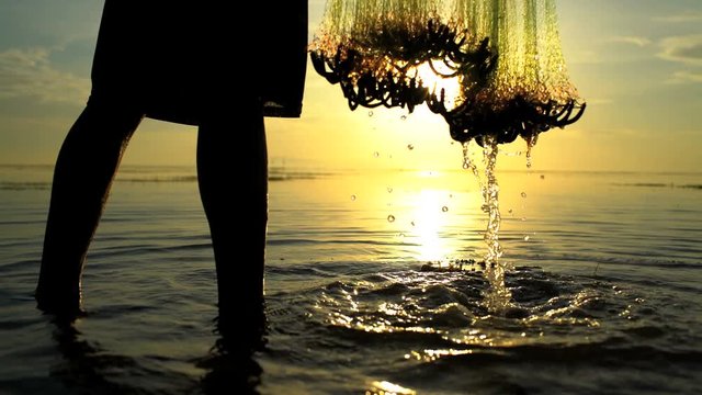 Balinese fisherman in silhouette throwing net into the ocean on a sunset beach