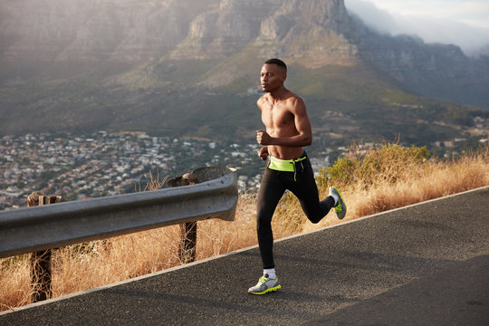 Healthy lifestyle banner panorama. Fast African American man has cardio running, poses outside, wears leggings and sneakers, enjoys speed, fresh air in rocky mountains. Exercising in open air.