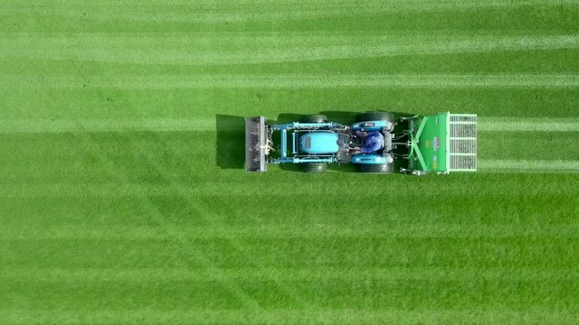 Large Lawn mower cutting green grass in a Soccer field - Top down aerial footage