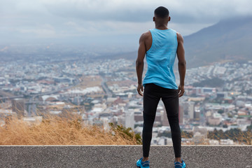 People, freedom, lifestyle concept. Back view of sporty man in sportsclothes, stands high on road,...