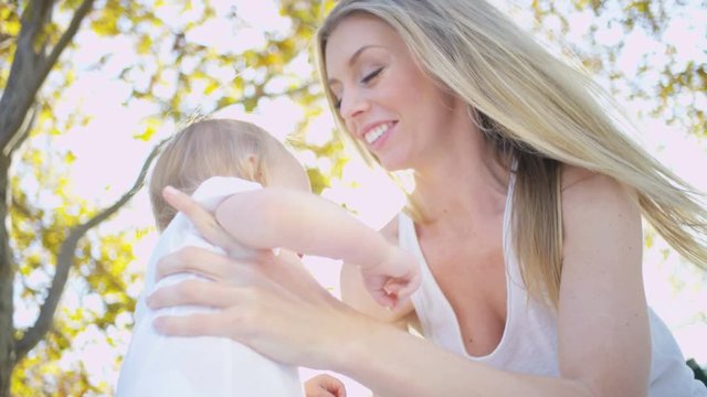 Cute blonde baby son bouncing up and down outdoors while his loving mother holds him 