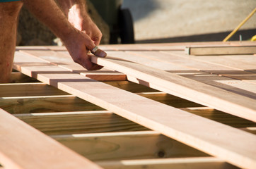 Man placing a plank of wood in a deck home renovation - obrazy, fototapety, plakaty