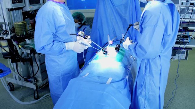 Surgical hospital Laparoscopic Operation carried out by Caucasian male and female specialist team in scrubs using monitors with African American Anesthesiologist 