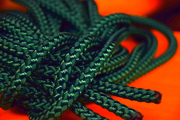 green nylon rope with focus to the ends in front of orange background, new green rope macro shot for the shipping or health or sports industry