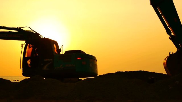 Construction Video At construction site The silhouette excavator is digging ground and lifting a large mortar, with engineering and construction workers to help with colorful sunset .