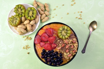 Breakfast with muesli, acai blueberry smoothie and kiwi, fruits on green background. Healthy food concept. Flat lay, top vie