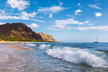 Makua beach view of the wave with beatiful mountains and a sailboat in the background, Oahu island, Hawaii