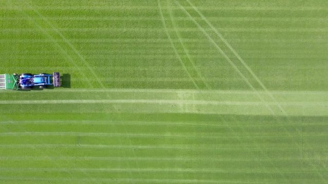 Large Lawn mower cutting green grass in a Soccer field - Top down aerial footage