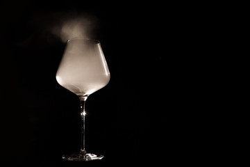 Burgundy crystal transparent red wine glass fully filled with white thick smoke, isolated close up on black background in the studio. Chemical party concept