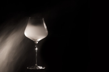 Burgundy crystal transparent red wine glass half filled with cold white thick smoke, isolated close up on a black background in the studio. Wine tasting concept