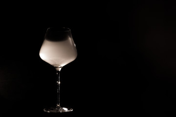 Burgundy crystal transparent red wine glass half filled with white thick smoke, isolated close up on a black background in studio. Wine tasting concept