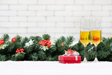 Two champagne glasses setting next to a red gift box on snowy table decorate with pine branches,...