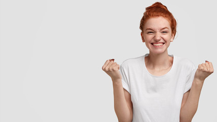 Studio shot of pleasant looking happy girl rejoices from excitement, celebrates excellent news,...