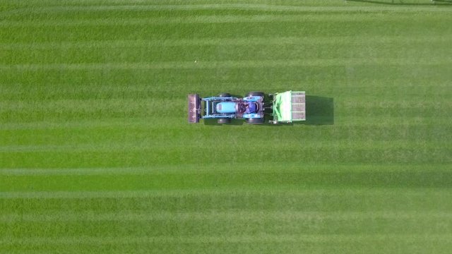 Large Lawn mower cutting green grass in a Soccer field - Top down aerial footage