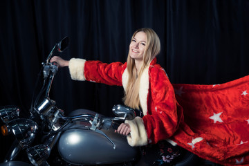 Fototapeta na wymiar Beautiful blonde in Santa Claus outfit on a motorcycle carries gifts