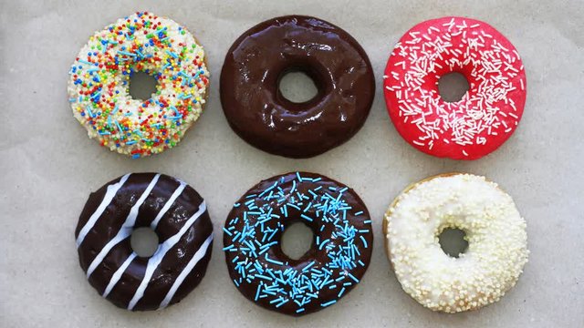 Donuts of different colors on cardboard, top view, stop motion animation. Full HD