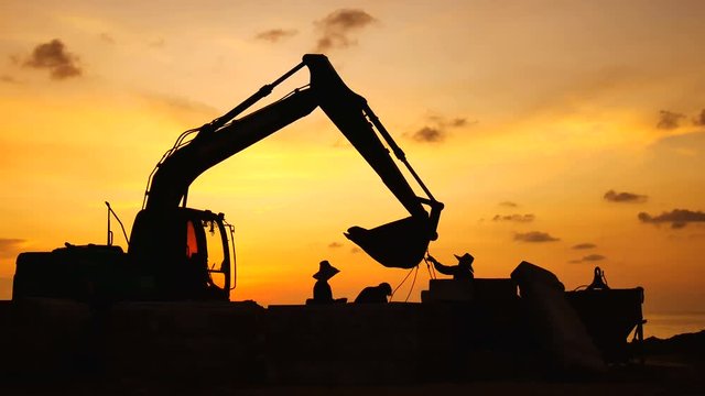 Construction Video At construction site The silhouette excavator is digging ground and lifting a large mortar, with engineering and construction workers to help with colorful sunset .