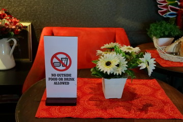 closeup of rectangular sign read no outside food or drink allowed, on red cloth with artificial flowers on round wooden table