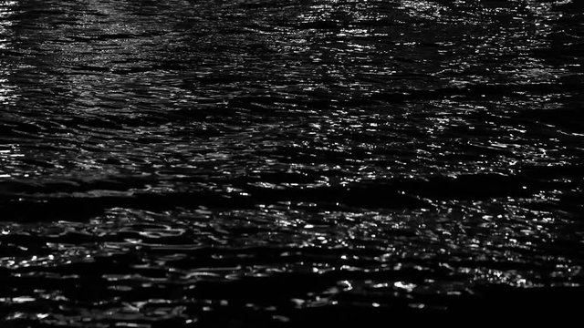 Black night sea water background with light reflections on calm surface. Real time 4k video footage.