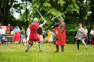 Fototapeta premium People wearing knight costumes fight during historical reenactment on annual Medieval Festival, held in Trakai Peninsular Castle.