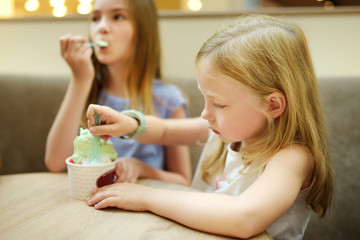 Obraz na płótnie Canvas Cute girls eating tasty fresh ice cream indoors. Children eating sweets.