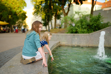 Two cute little girls playing by city fountain on hot and sunny summer day. Children having fun with water in summer.