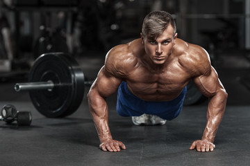 Muscular man working out in gym doing push-ups exercises, strong male naked torso abs