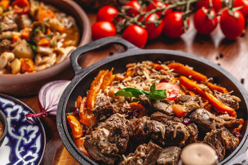 The concept of Uzbek, oriental cuisine. Pilaf in a cast-iron pan, with pieces of lamb lies on a wooden table. Festive table set.