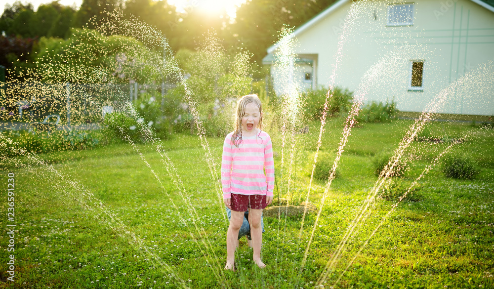 Canvas Prints Adorable little girl playing with a sprinkler in a backyard on sunny summer day. Cute child having fun with water outdoors.