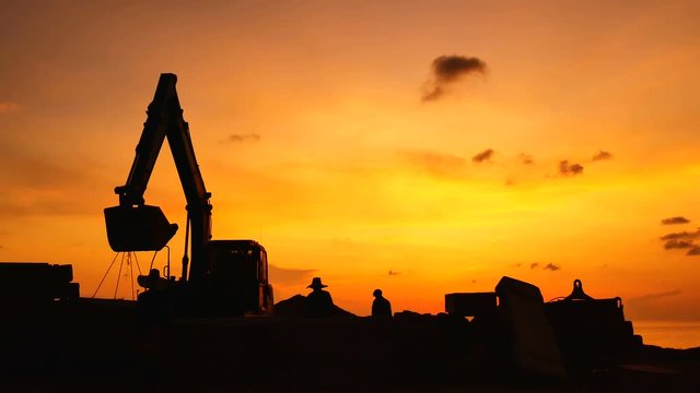Construction Video At construction site The silhouette excavator is digging ground and lifting a large mortar, with engineering and construction workers to help with colorful sunset .