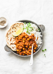 Indian spicy chickpeas curry with rice and naan bread in pan on light background, top view. Healthy delicious vegetarian food