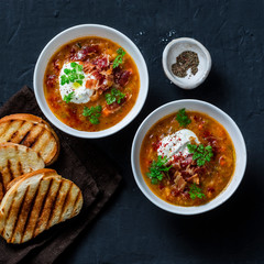 Multi grain and vegetables soup with grilled cheese sandwiches and crispy bacon on a dark background, top view. Delicious comfort food concept. Flat lay