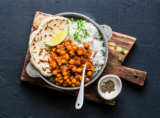 Indian spicy chickpeas curry with rice and naan bread in pan on dark background, top view. Healthy...