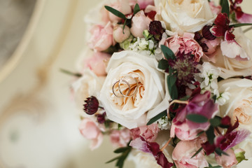  Bridal bouquet of white roses and burgundy orchids on the table and wedding rings close up 