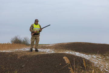 Hunter with a gun and a dog go on the first snow in the steppe, Hunting pheasant in a reflective...