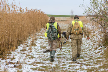 Hunter with a gun and a dog go on the first snow in the steppe, Hunting pheasant in a reflective vest	