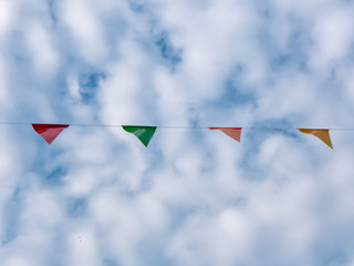 Row of colorful triangles flags on blue sky with clouds background in carnival fair