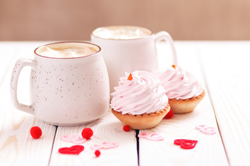 Two cups of coffee and cupcakes with pink cream for Valentine's Day or Birthday, wedding day. White wooden background. Selective focus