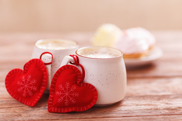 Background romantic mood. Two cups of coffee with decorative felt hearts for Valentine's Day or Birthday, wedding day. Wooden background. Cakes on blurred background. Selective focus, close-up