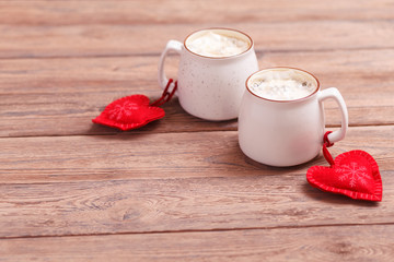 Background of romantic mood. Two cups of coffee with decorative felt hearts tied on the handles for Valentine's Day or wedding day. Wooden background. Selective focus, close-up, copy space