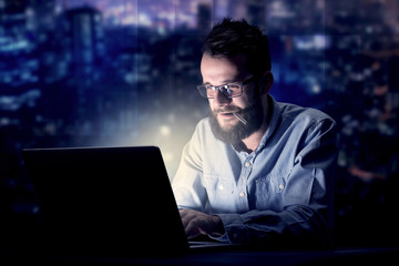 Young handsome businessman working late at night in the office with blue lights in the background