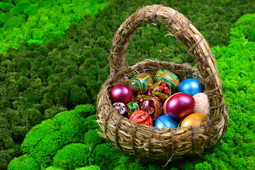 Easter background. Holiday decorative eggs in a basket on a green moss backdrop.