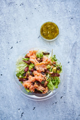 A delicious smoked salmon take away salad with smoked salmon, lettuce, mixed baby greens, beans, dry tomatoes, cherry tomatoes and red onion with green sauce.