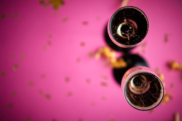 Two glasses full of sparkling champagne wine with golden decoration of confetti and serpentines on pink background. Top view with copy space. Festive or party concept.
