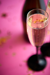 Bottle and two glasses full of sparkling champagne wine with golden decoration of confetti and serpentines on pink background. Top view with copy space. Festive or party concept.