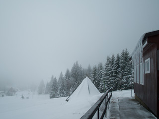 Cottage with icicles and forest in a background, cloudy weather. Winter in the Giant Mountains, Czech Republic.